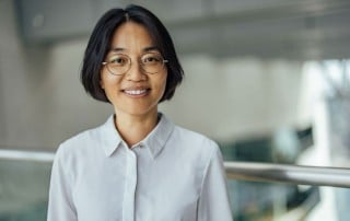 Woman with dark hair and glasses looking into camera and smiling