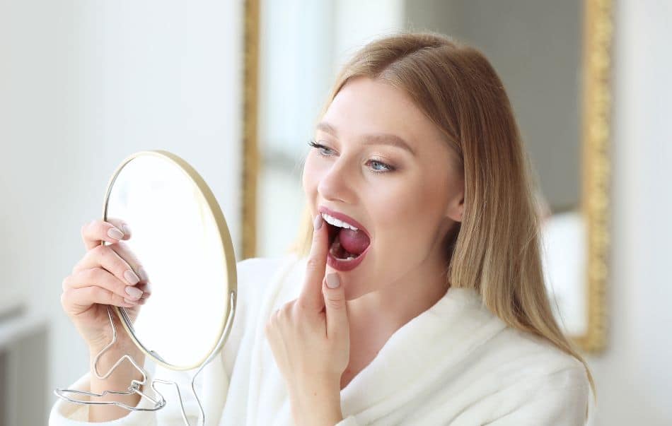 A woman examining her teeth in a small hand mirror